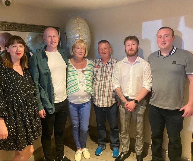 Six members of the Sharkey family standing together indoors, smiling for the camera.